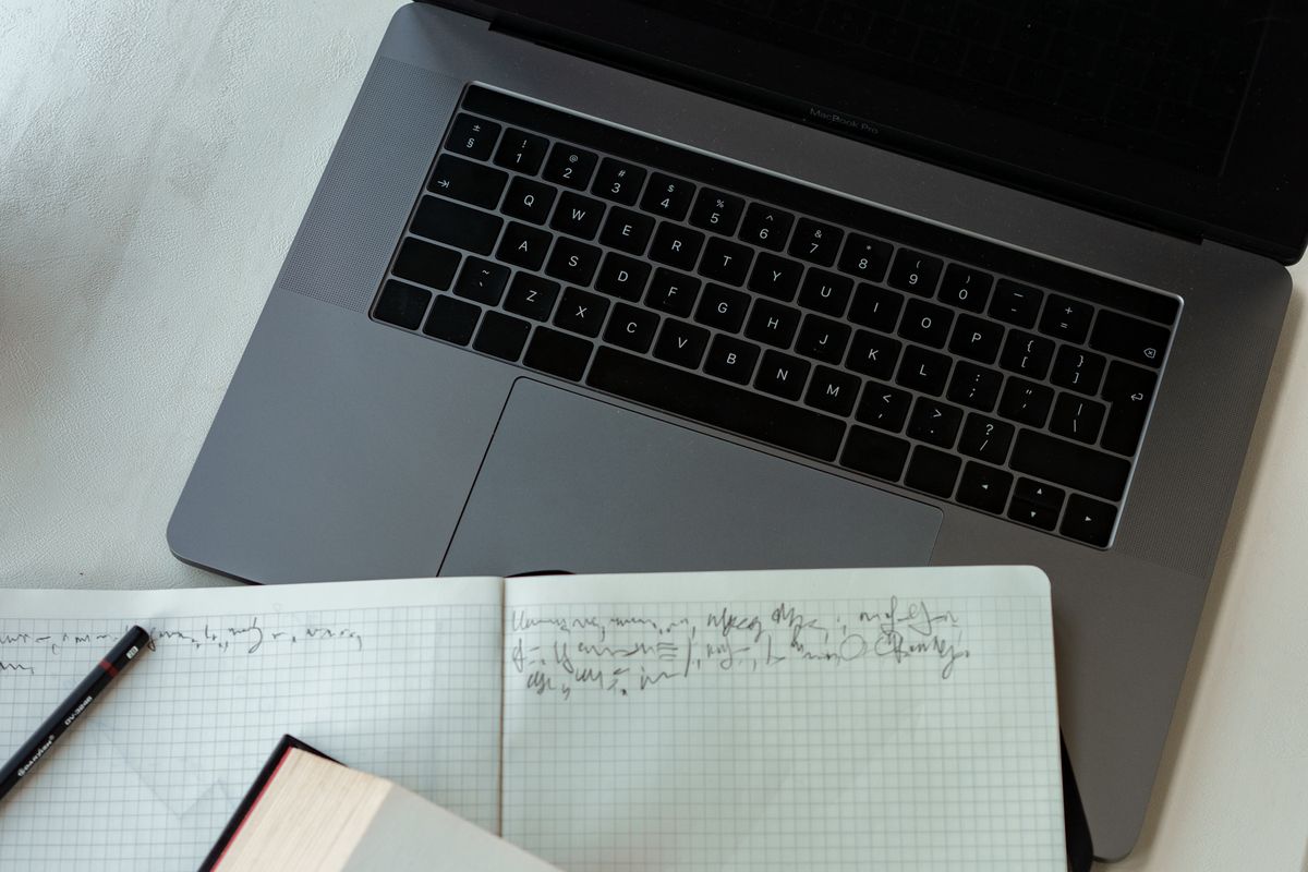 ノートパソコンと手書きのノート、書籍が並ぶ机の上